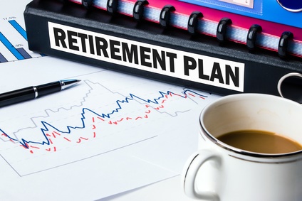 This image shows a black binder with the word Retirement on its side, a pen, a coffee cup, and a financial graph on a desk.